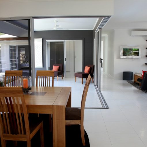 A spacious and modern dining room inside an energy-efficient home in Ireland, featuring large sliding glass doors for natural light, sleek white floor tiles, and wooden furniture with orange accents