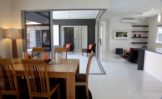 A spacious and modern dining room inside an energy-efficient home in Ireland, featuring large sliding glass doors for natural light, sleek white floor tiles, and wooden furniture with orange accents