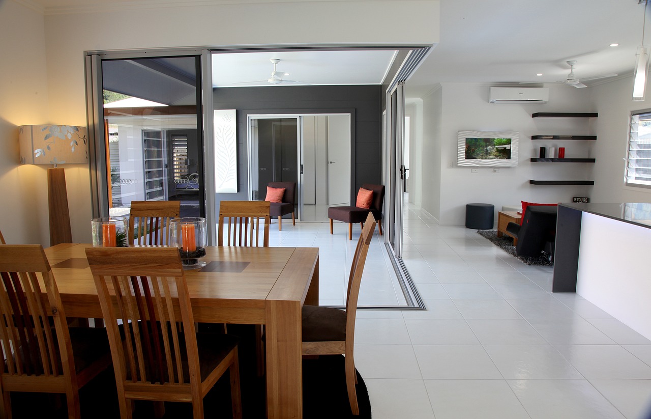 A spacious and modern dining room inside an energy-efficient home in Ireland, featuring large sliding glass doors for natural light, sleek white floor tiles, and wooden furniture with orange accents