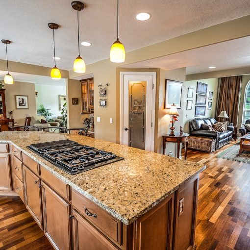 Modern kitchen renovation featuring an island with a granite countertop and built-in gas cooktop, surrounded by wooden cabinetry and hardwood floors, leading into an inviting living room with comfortable seating and large windows.