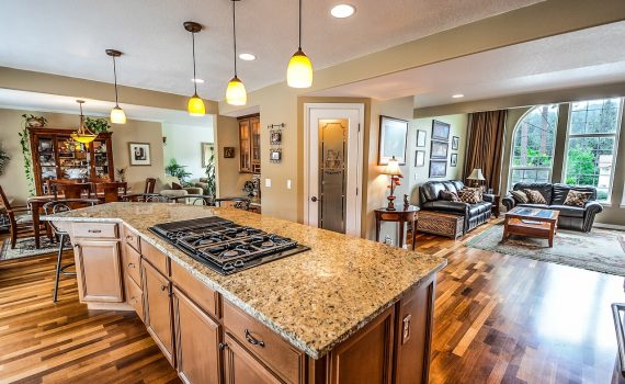 Modern kitchen renovation featuring an island with a granite countertop and built-in gas cooktop, surrounded by wooden cabinetry and hardwood floors, leading into an inviting living room with comfortable seating and large windows.